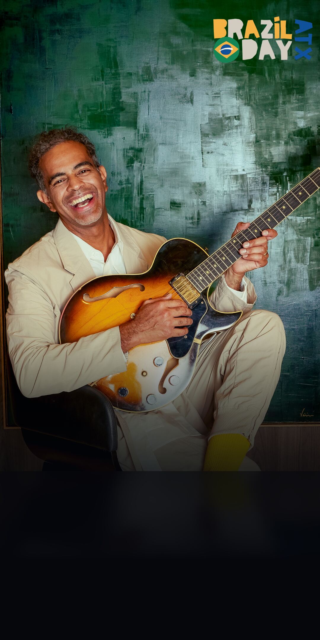 Jair Oliveira laughing while playing a hollow-body electric guitar
