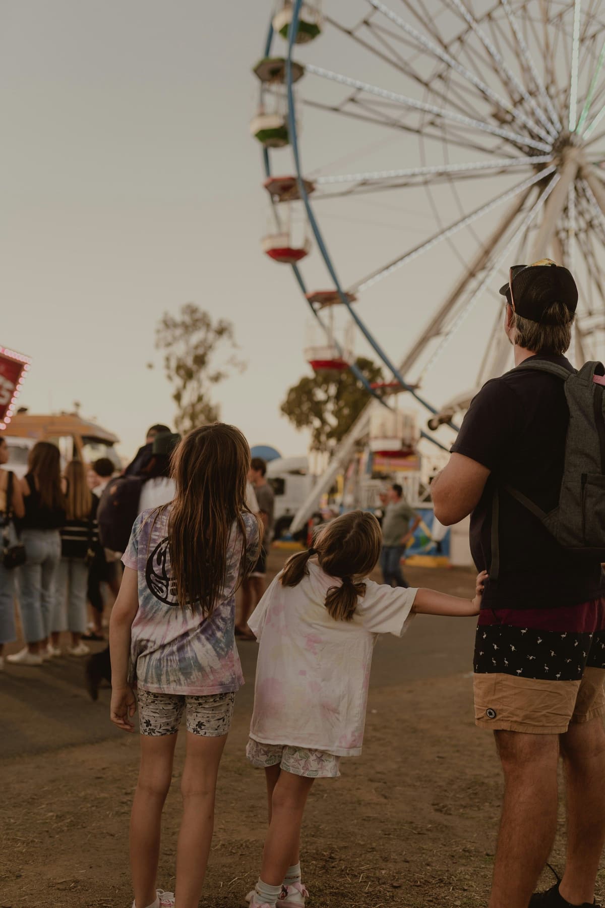 Two girls and an adult looking up at a Ferris wheel at the fair