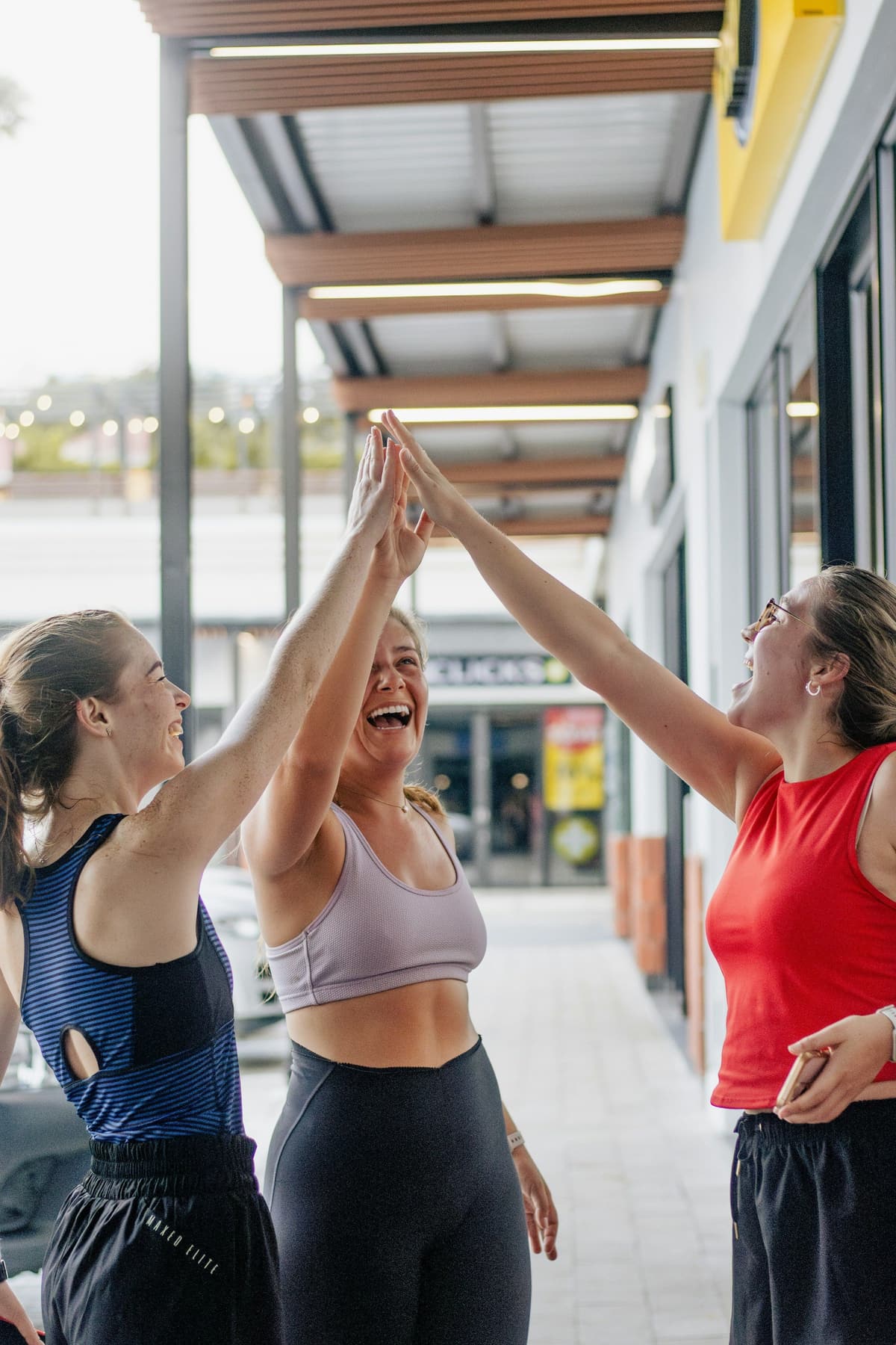 Three women laughing and high-fiving after a workout