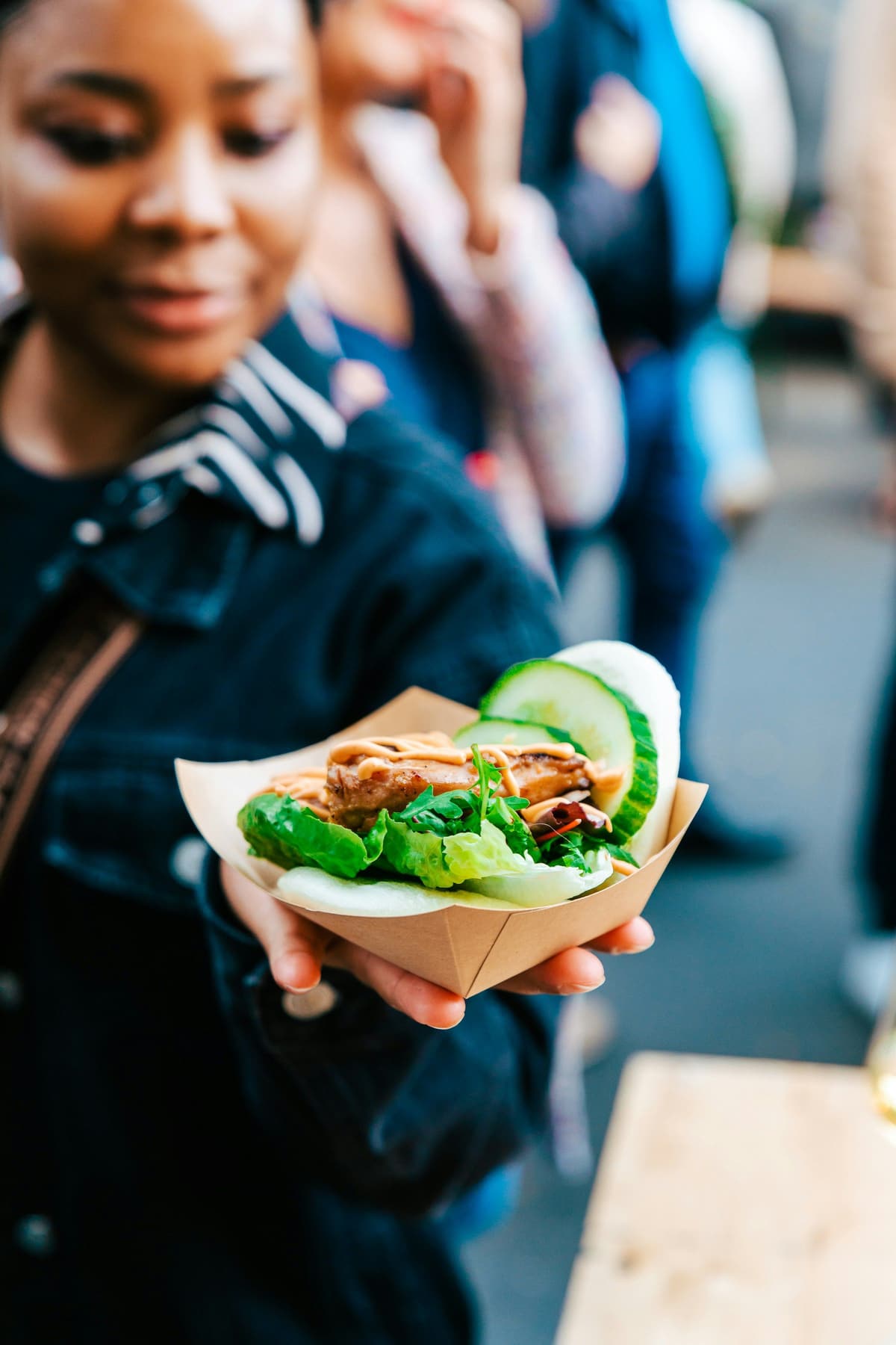 A woman holding out a bao bun at a street food market