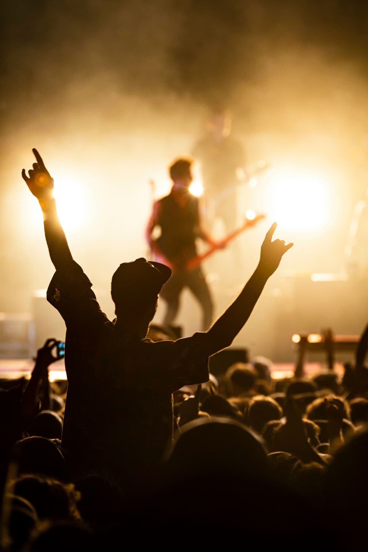 A fan with both arms up in front of a backlit band on stage