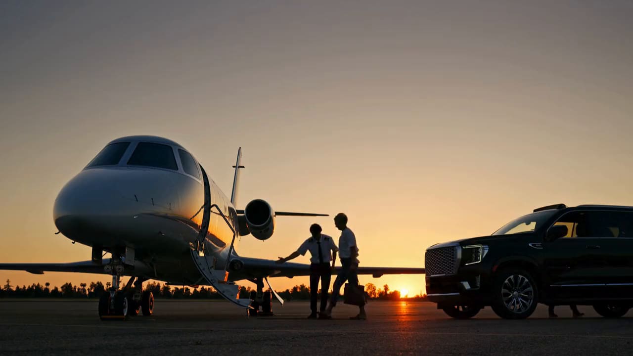 A black SUV waiting beside a private jet at sunset
